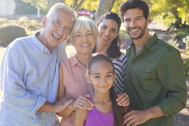 Family members of different generations smiling and standing close together in a park. Ideal for use in advertisements, family-oriented content, lifestyle blogs, and promotional materials emphasizing family values and togetherness.