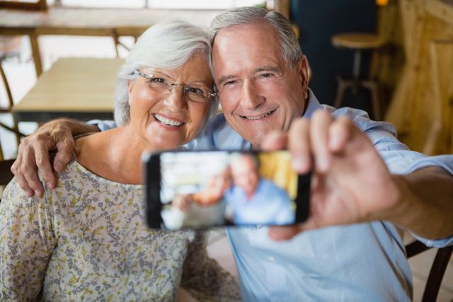Senior couple enjoying time together in a cafe, capturing a happy moment with a selfie. Ideal for use in advertisements, articles, or blogs about senior lifestyle, relationships, retirement, and leisure activities.