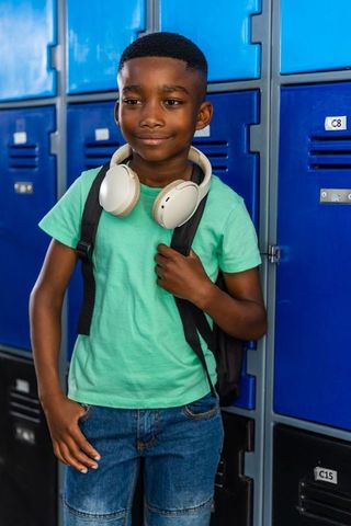 African american boy standing by school lockers wearing headphones and backpack