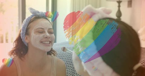 Smiling woman receiving facial mask and brush while wearing soft headband with rainbow heart