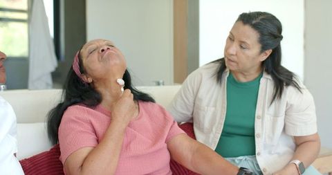 African american caregivers assisting senior woman using sore throat lozenge while sitting on sofa