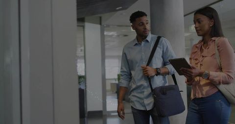 Two colleagues walking and consulting tablet in modern office corridor for agile teamwork