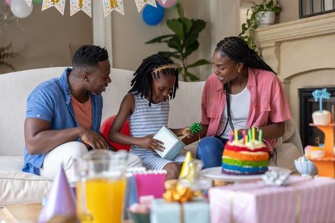 African american family celebrating birthday at home with child opening gift on sofa
