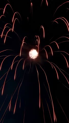 Vertical fireworks bursting and sending red-orange spark trails across black night sky