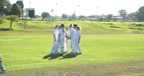 Female cricket team huddling in sunlit field for team spirit