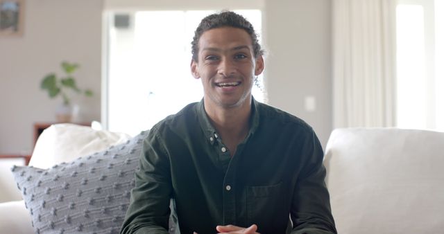 Young man smiling confidently while sitting in bright living room - Download Free Stock Images Pikwizard.com