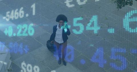 Walking businesswoman pulling suitcase talking on smartphone with financial data overlay
