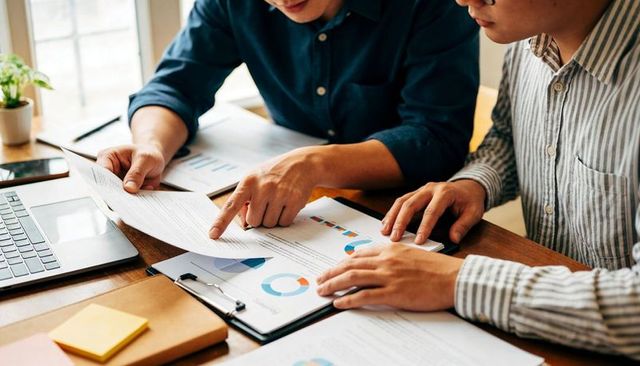 Two colleagues reviewing financial charts and business reports at shared desk during meeting