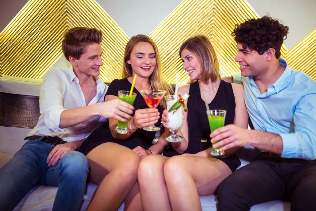 Joyful friends toasting cocktail glasses at nightclub