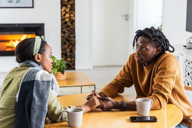 African american couple holding hands, talking at table in cozy living room