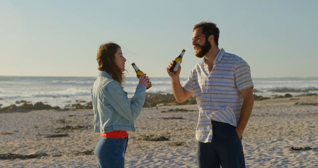Young couple enjoying beer while relaxing on sandy beach. Ideal for marketing materials related to beverages, beach vacations, friendships, and summer casual lifestyles. Suitable for travel brochures, beverage ads, and social media promotions.