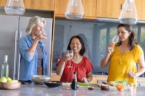 Multigenerational friends toasting with wine while cooking together in modern kitchen
