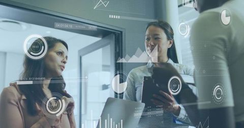 Businesswomen Collaborating Over Interactive Data Dashboards in Modern Glass Office