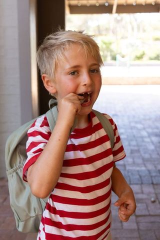 Young boy losing baby tooth while wearing backpack on school porch
