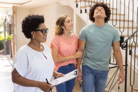 Realtor showing modern home to diverse couple exploring sunlit staircase