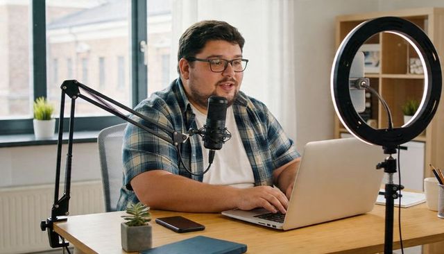 Podcast host recording livestream with laptop, microphone and ring light in home office