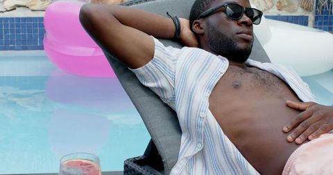 Relaxing man lounging poolside wearing sunglasses with citrus drink and pool float