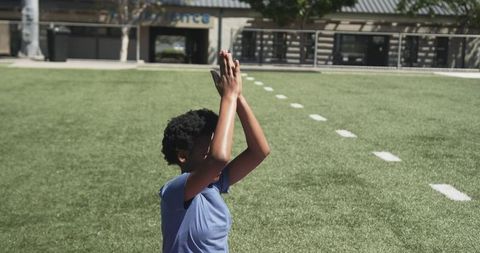 Teen raising arms on sunny turf field wearing sunglasses and blue athletic t-shirt solo