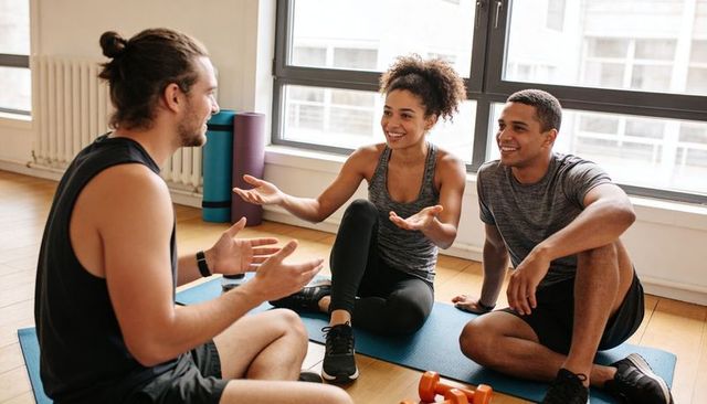 Fitness instructor coaching smiling group on mats in bright studio with dumbbells