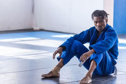 Martial artist in blue gi sitting on dojo mats