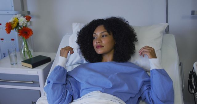 Biracial woman lying in hospital bed fluffing her pillow. medicine, health and healthcare services.