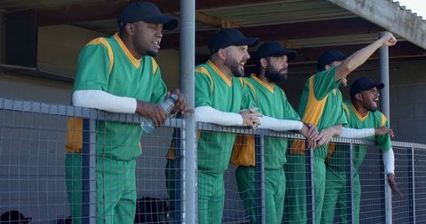 Multiracial baseball team cheering from dugout wearing green and yellow uniforms