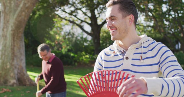 Father and Son Smiling and Raking Leaves in Sunny Park - Download Free Stock Images Pikwizard.com