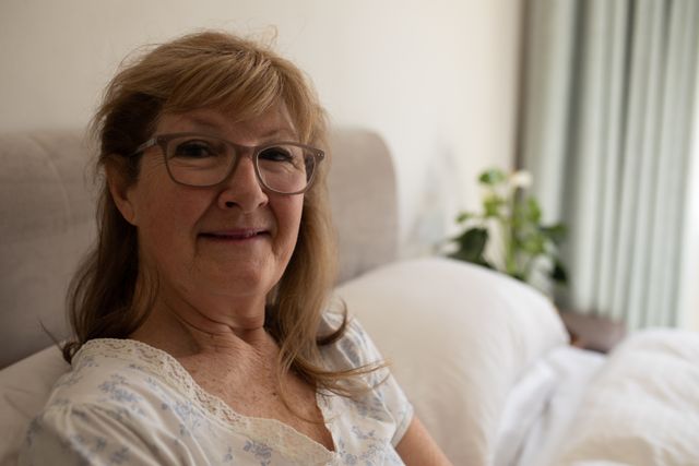 Senior woman lying in bed, smiling and looking happy. Ideal for use in articles or advertisements related to elderly care, health and wellness, home life, and the impact of Covid-19 quarantine on seniors. Can also be used in content promoting positive aging and mental well-being.