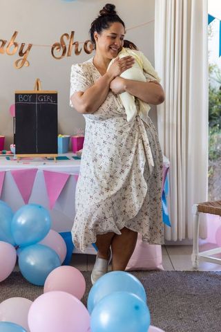 Mid adult woman cradling infant at home baby shower celebration