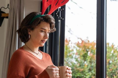 Woman wearing reindeer headband holding mug by sliding door in soft morning daylight