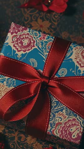 Vertical close-up showing hands untying red ribbon on patterned gift box, unwrapping moment