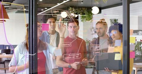 Team brainstorming and sketching on glass whiteboard in modern coworking space