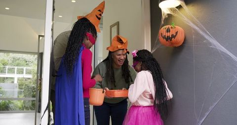 Diverse family welcoming costumed children on decorated porch holding halloween treats