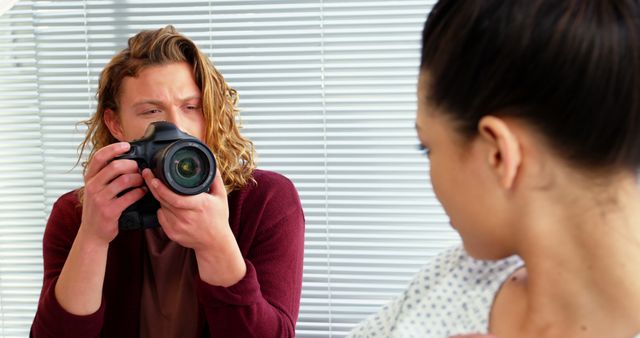 A young Caucasian male photographer is taking a picture of a woman, with copy space. His focused expression and her pose suggest a professional photoshoot in progress.