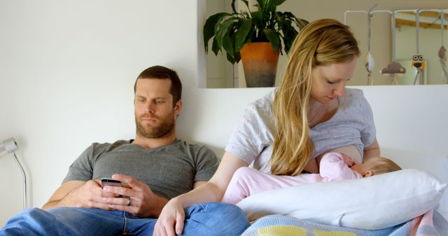 Mother Breastfeeding Baby While Father Uses Smartphone on Couch - Download Free Stock Images Pikwizard.com