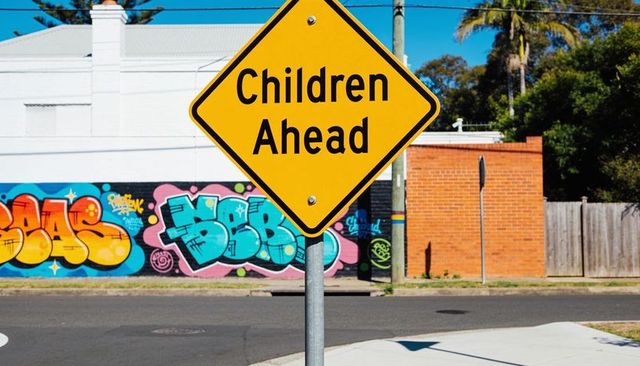 Yellow children ahead sign on urban corner with colorful graffiti mural and palm trees