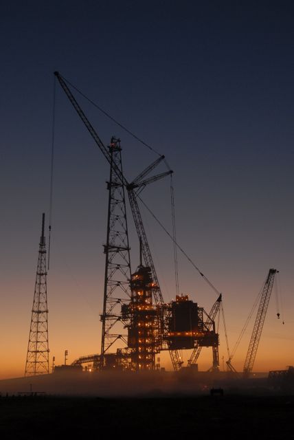 The photo captures the construction of new lightning towers at dawn in Cape Canaveral, part of NASA's Kennedy Space Center. The image highlights the towering structures being built to protect the Ares I rocket launches. Use this image for topics related to space exploration, NASA, engineering challenges, or early morning construction projects at significant aerospace locations.