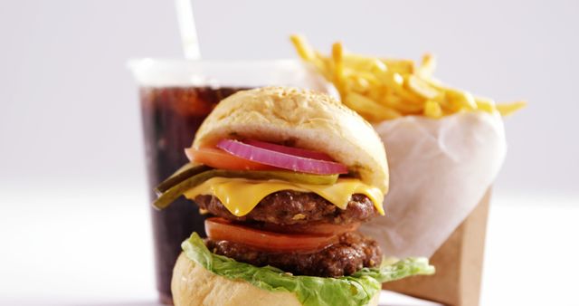 A cheeseburger with lettuce, tomato, pickles, and onions is paired with a side of fries and a soft drink, with copy space. Fast food meals like this are popular for their convenience and taste, despite health considerations.