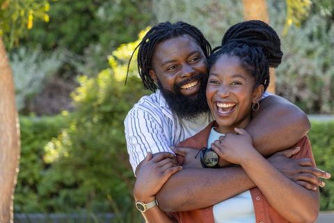 Sunlit african couple embracing and laughing in park, joyful outdoor portrait dreadlocks