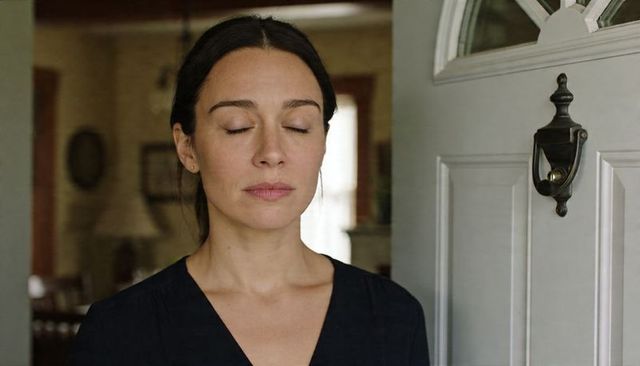 Woman standing at doorway closing eyes, finding calm beside paneled door with knocker