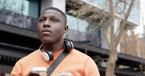 African American Commuter Wearing Headphones Holding Coffee and Pastry in Urban Plaza