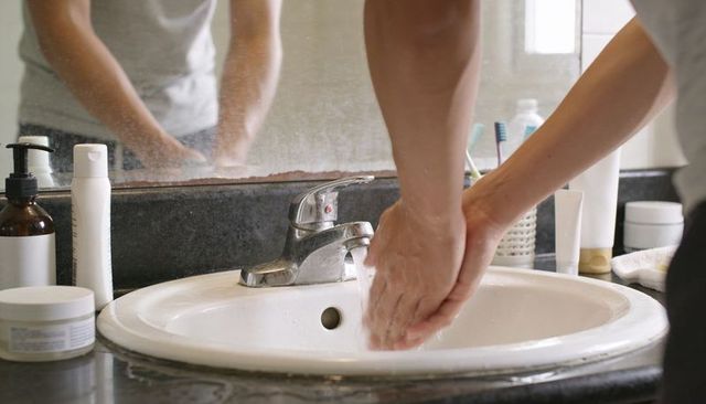 Washing hands at bathroom sink with chrome faucet, soap pump and mirror reflection