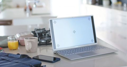 Silver laptop sitting on bright kitchen island with coffee and smartphone for remote work