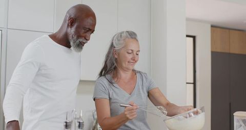 Mature couple cooking together in modern kitchen whisking batter and sharing moment