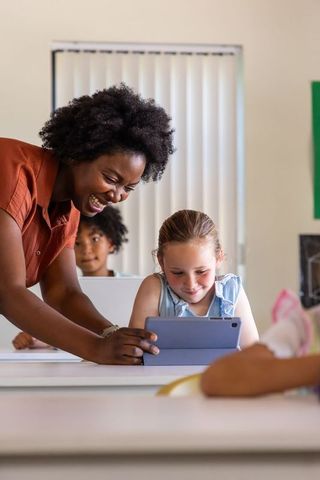 African American Teacher Guiding Elementary Student on Tablet in Bright Classroom