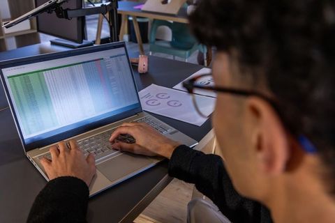 Asian man working on spreadsheet on laptop in modern coworking space with pink headphones
