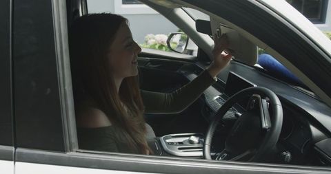 Young woman checking sun visor mirror in parked car while preparing for drive