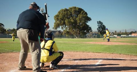Youth baseball catcher squatting with umpire and pitcher preparing pitch at sunny ballpark
