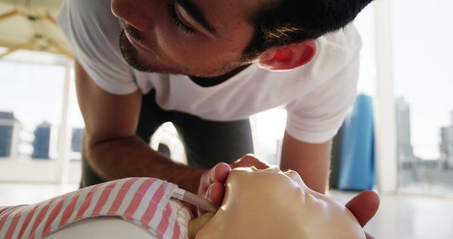 Man practicing CPR on a training manikin in a bright, sunny room. This image could be used in educational materials, healthcare training programs, emergency response courses, and resources promoting first aid awareness. Perfect for illustrating CPR training, emergency preparedness, and medical simulation in professional or classroom settings.