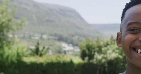 Smiling african boy showing missing front tooth in sunny garden with valley background